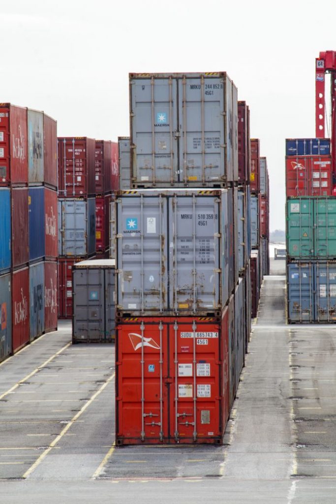 pexels-photo-14617647 Vertical shot of colorful shipping containers stacked at an industrial port, showcasing logistics.
