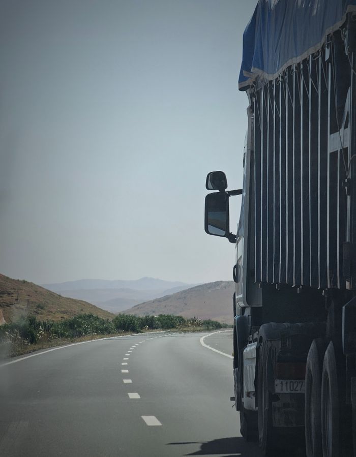 pexels-photo-16180770 Truck on a winding highway in Douar Ouled El Mesnaoui, Morocco, set in a rocky landscape.